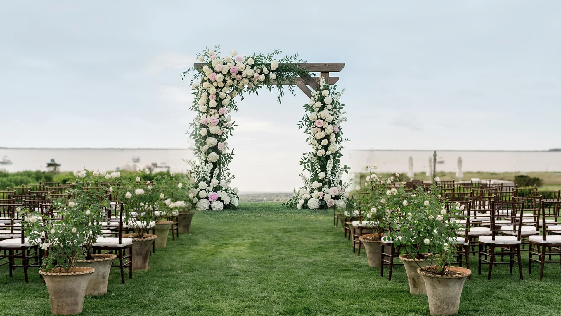 Potted saplings lining a ceremony entrance, simple white chairs beyond.